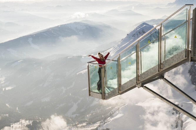 Person on glass skywalk extending over snow-capped mountains