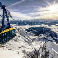 Yellow and blue gondola car labeled Der Dachstein over snow-covered mountains