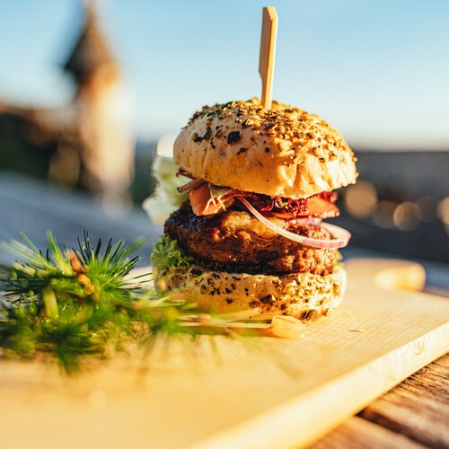 Stacked burger with sesame bun, onions, lettuce on board | © Christine Höflehner