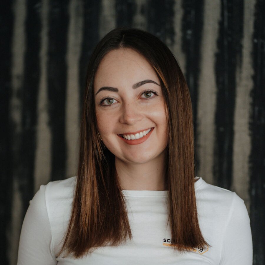 Smiling woman with long brown hair in white top and black belt