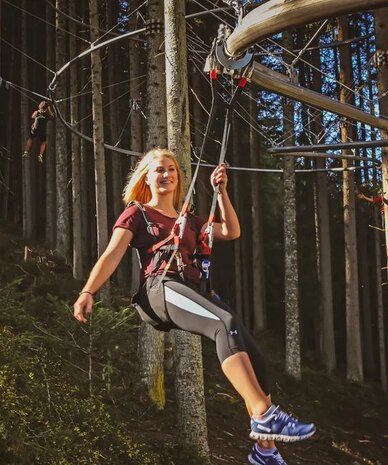 Person on a zipline in a dense forest wearing a harness