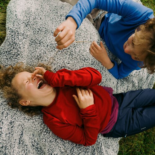 Two children laughing, lying on a shaggy gray blanket outdoors