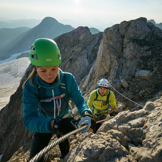 Two climbers ascend a rocky mountain ridge using a rope