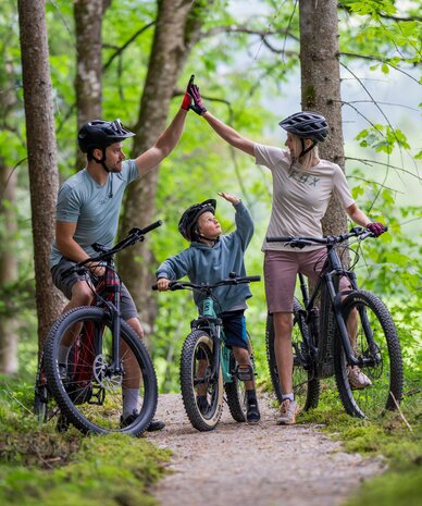 Family of three high-fiving on a forest bike ride