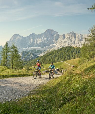 Two cyclists ride along a gravel trail in alpine scenery