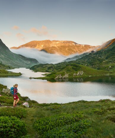 Two hikers trek through alpine meadow beside a lake