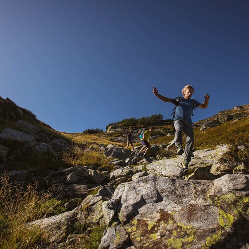 Hikers traverse a rocky mountain trail beneath a clear blue sky
