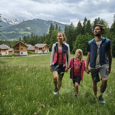 Family walking hand in hand through grassy alpine meadow | © RAPHAELGABAUER.COM