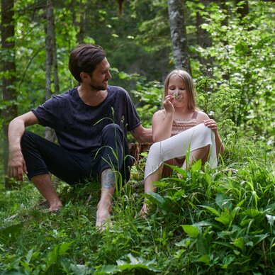 Man and girl sitting on grass in a green forest