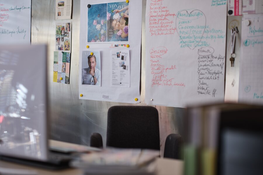 Office wall with posters, notes, and a chair | © RAPHAELGABAUER.COM