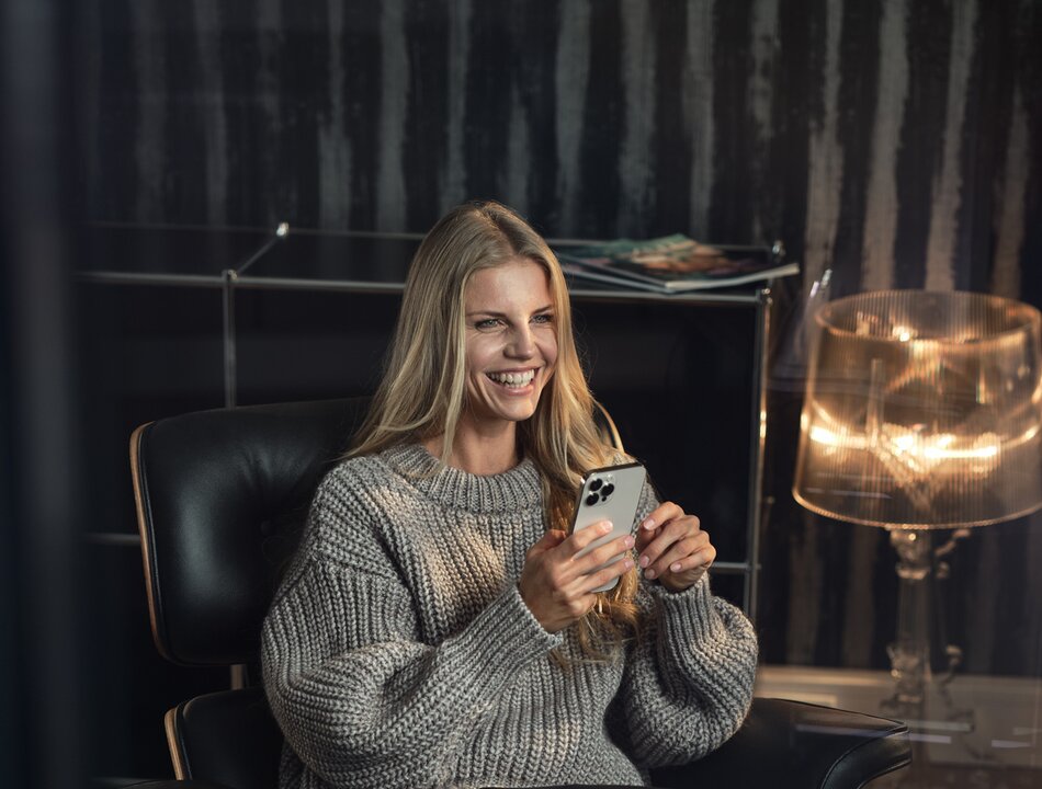 Smiling woman seated in a modern leather armchair using a smartphone | © RAPHAELGABAUER.COM