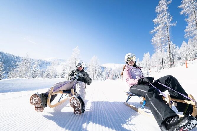 Two people sledding on wooden toboggans down a snowy slope