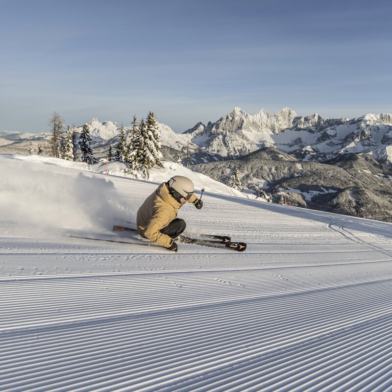 Skier carving on groomed slope with snowy mountains | © Mirja Geh