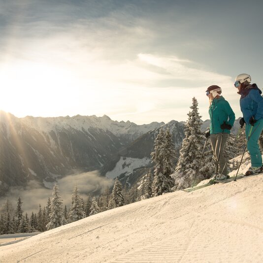 Two skiers in winter gear stand on snowy slope, mountains in background. | © Martin Huber