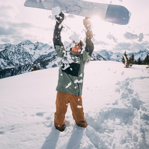 Person raises snowboard amid flying snow in mountains