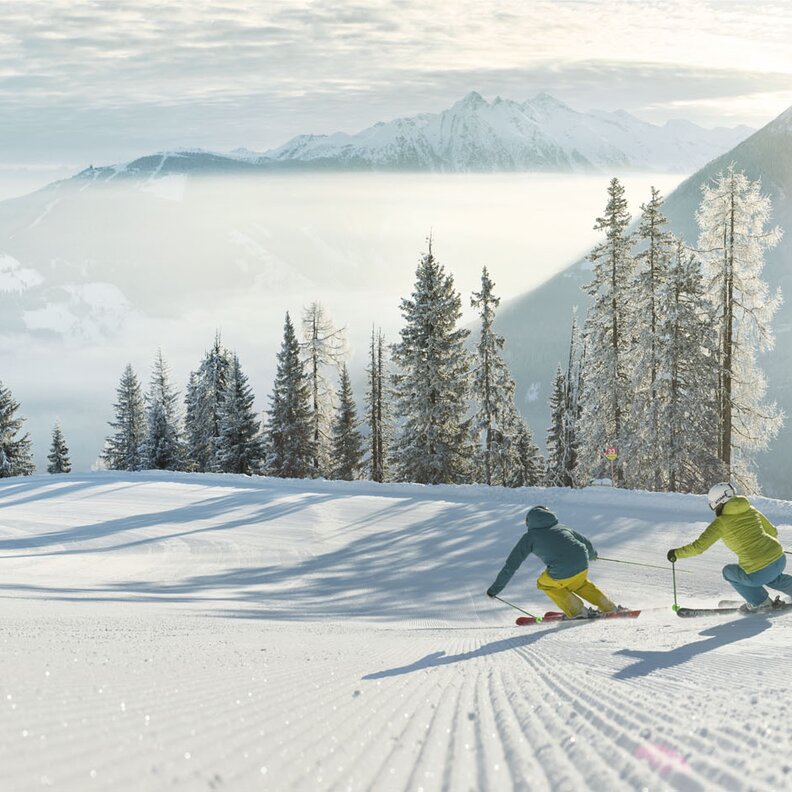 Two skiers carving turns on a snowy slope.