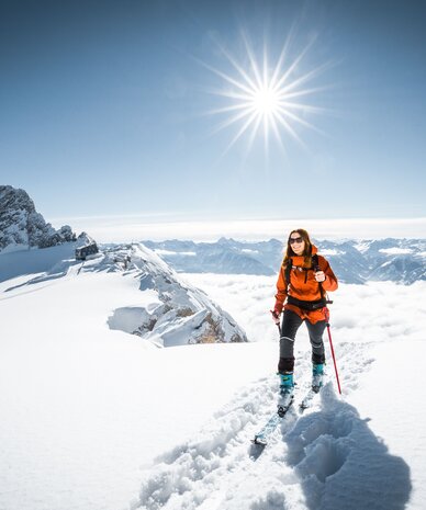 Skier in orange jacket on snowy mountain ridge with sun