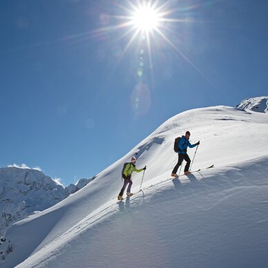 Two hikers ascend a snow-covered mountain slope under a bright sun. | © HERBERT RAFFALT
