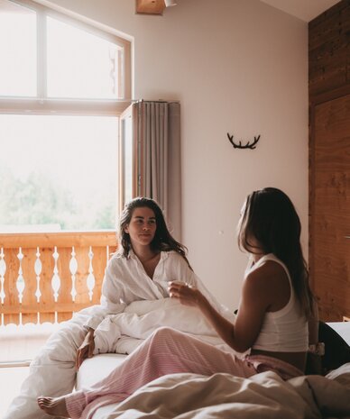Two women chat in sunlit bedroom