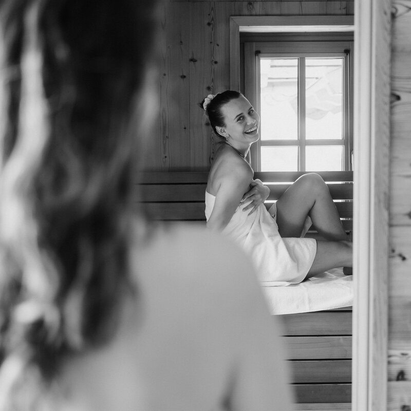 Smiling woman wrapped in towel sits on wooden bench.
