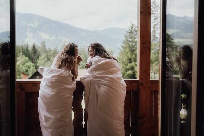 Two women in white bathrobes on balcony overlooking mountains