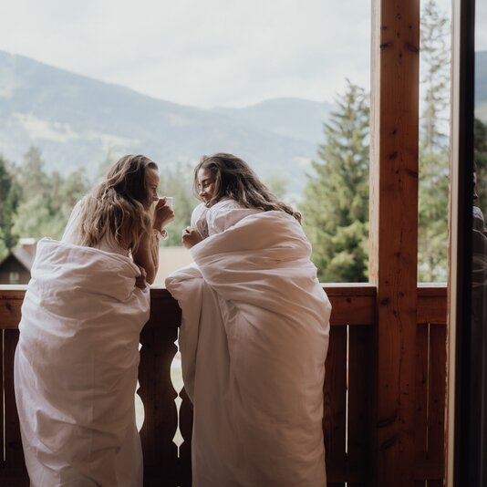 Two women in white bathrobes on balcony overlooking mountains