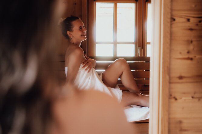 Smiling woman wrapped in a towel sits on sauna bench