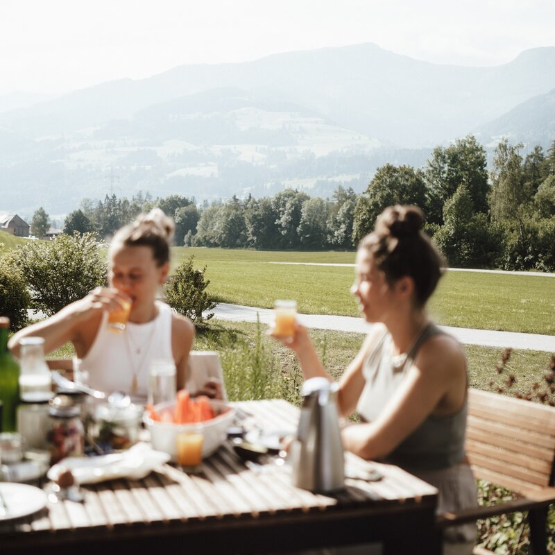 Two women sipping drinks at a rustic outdoor table.