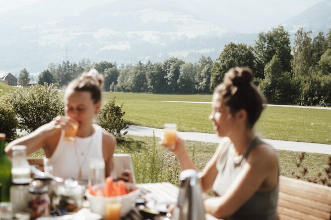 Two women sipping drinks at a rustic outdoor table.