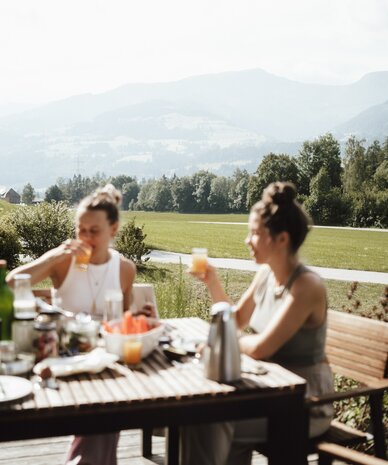 Two women sipping drinks at a rustic outdoor table.