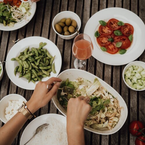 Hands tossing salad in a large bowl on a wooden table