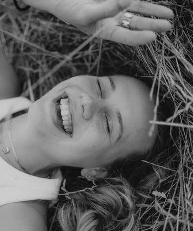 Smiling woman lying in grass with hand and rings visible