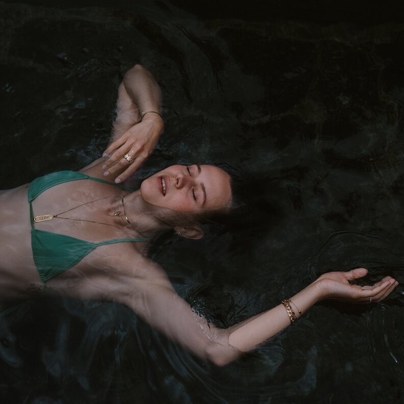 woman floating in dark water wearing a green bikini