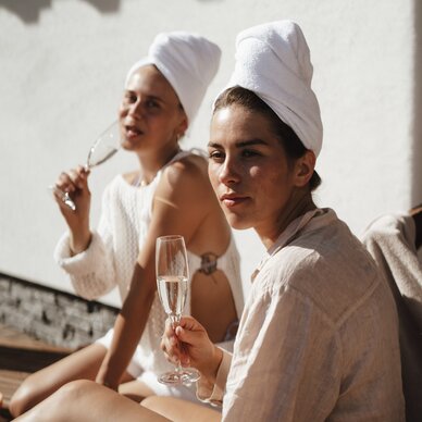 Two women in towels outdoors with champagne flutes