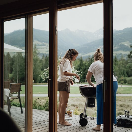 Two people grilling on a wooden deck with a mountain backdrop