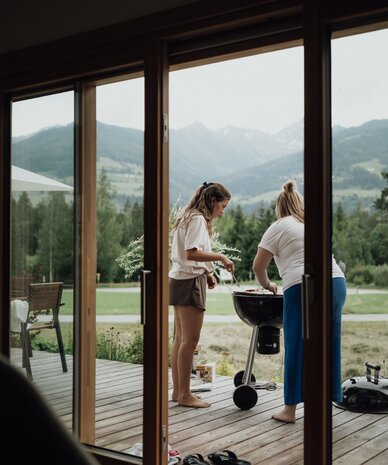 Two people grilling on a wooden deck with a mountain backdrop