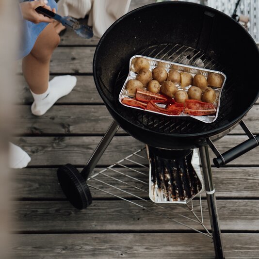 Barbecue grill on a wooden deck with potatoes and peppers tray