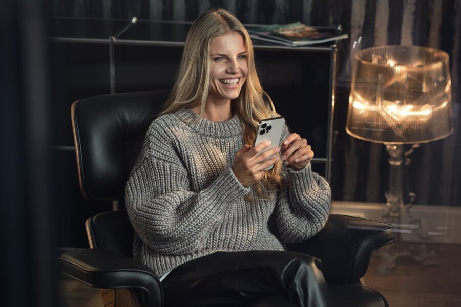 Smiling woman seated in a black leather armchair holds a smartphone | © RAPHAELGABAUER.COM