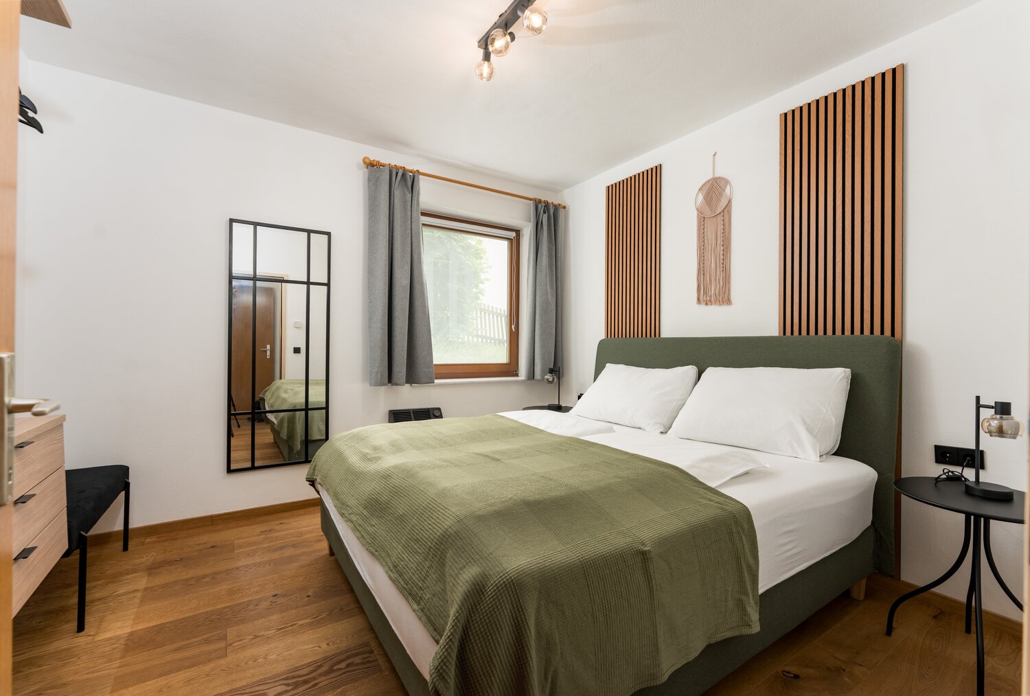 Double bed with green headboard and white pillows in modern bedroom.
