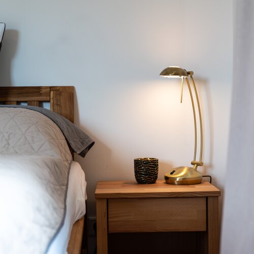 Wooden nightstand beside bed with brass lamp and cup