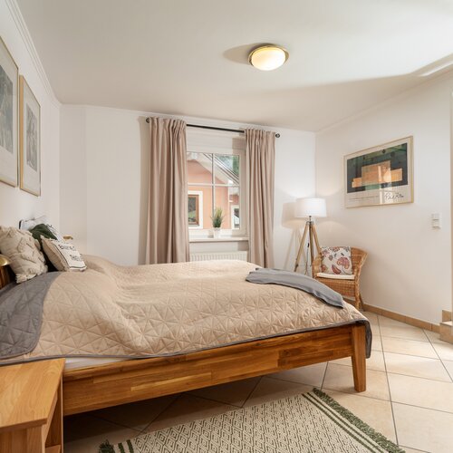 Bedroom with wooden bed, beige quilt, and wicker chair.