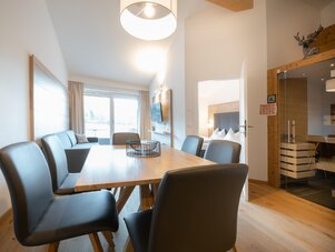 Open-plan dining area with wooden table, black chairs, and large window | © TIEBER