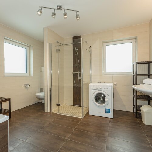 Modern bathroom with glass shower, toilet, sink, washer.