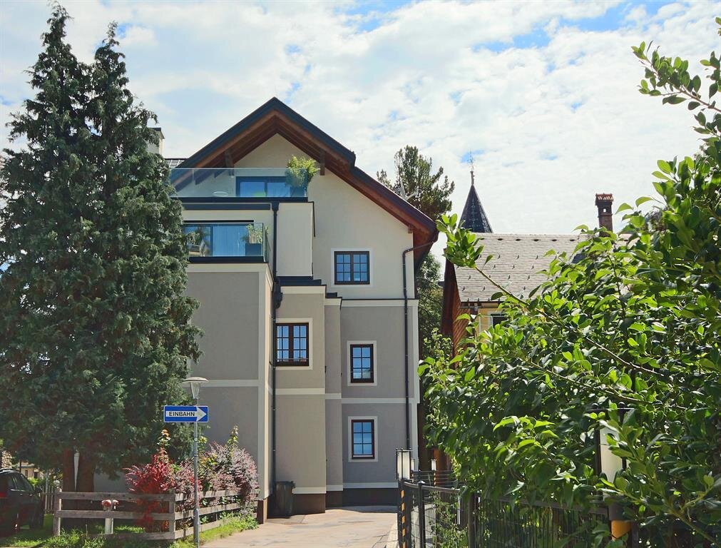 Three-story apartment building with trees and a one-way sign.