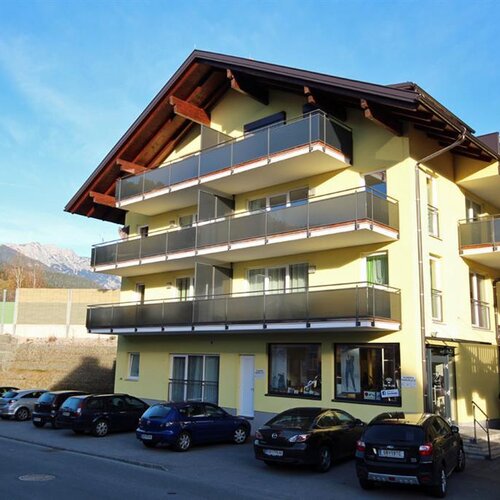 Yellow multi-story apartment building with balconies and parked cars