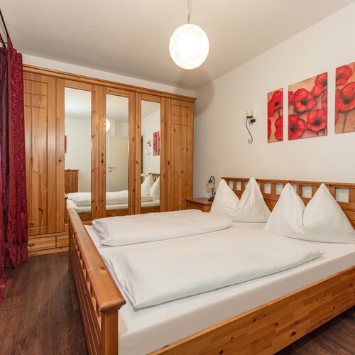 Wooden bed with white bedding, mirrored wardrobe, and pink curtains.