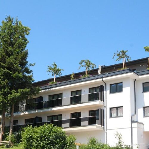 Modern white apartment building with balconies and trees