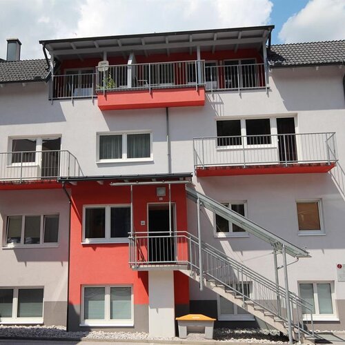 Multi-story residential building with red accent walls and exterior metal stairs.