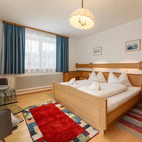 Bright hotel room with wooden double bed, seating area, and blue curtains