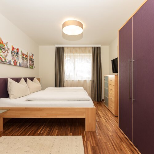 Hotel room with large bed, purple wardrobe, cat artwork